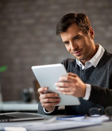 Happy entrepreneur using digital tablet and reading something while working in the office.